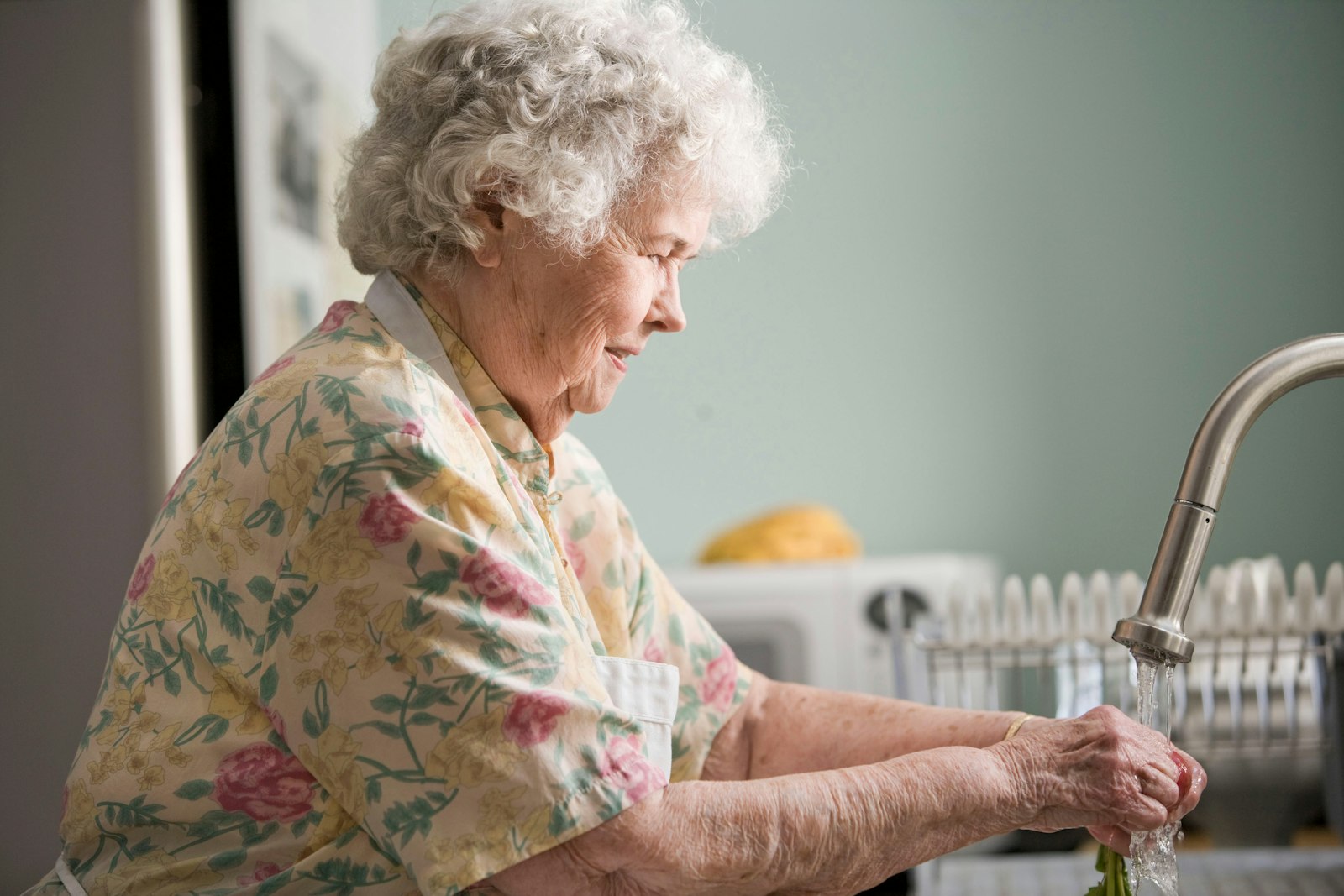 An elderly woman washing vegetables at her own kitchen sink
