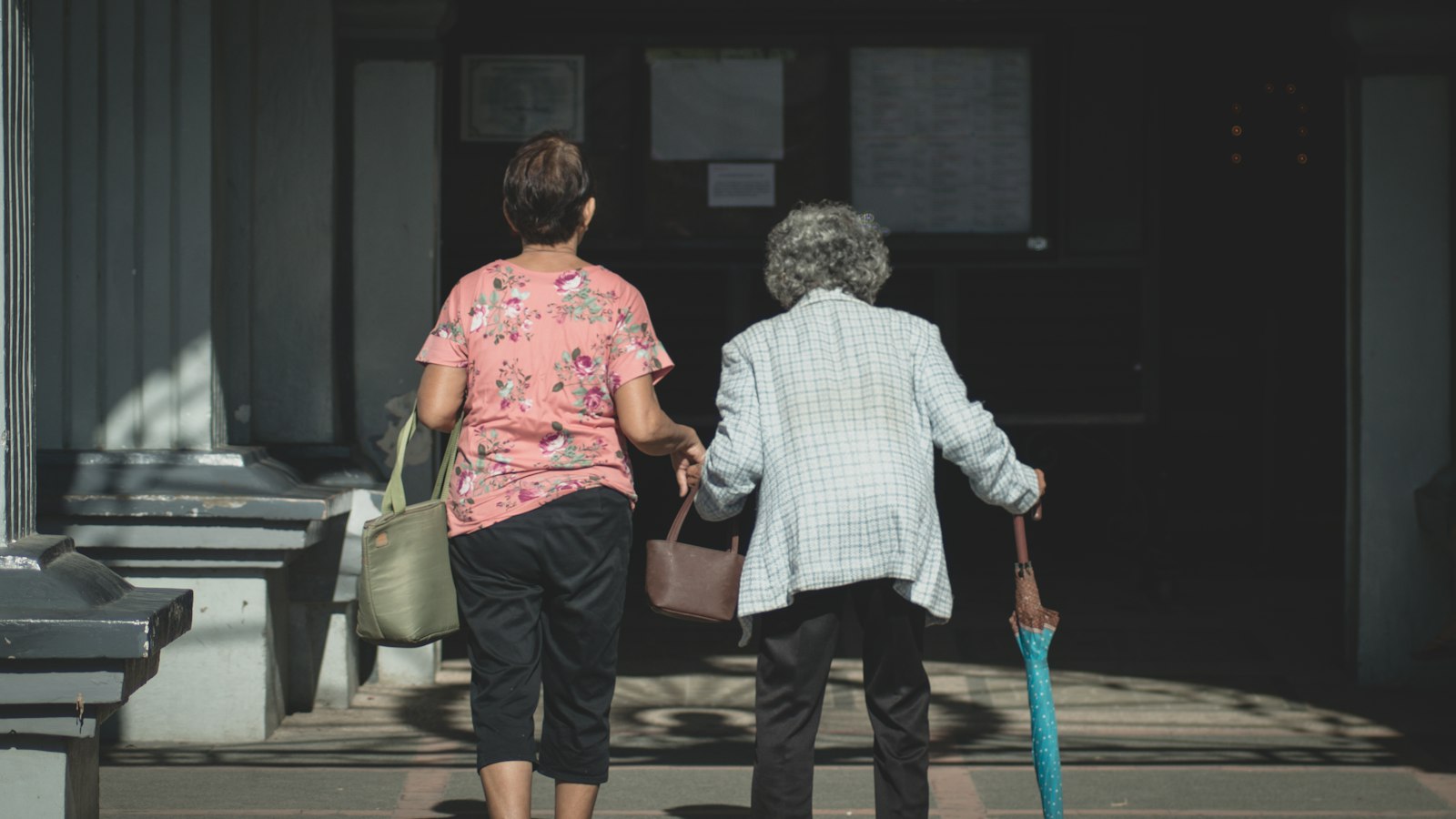 A daughter walking her elderly mother up to the front door of her home